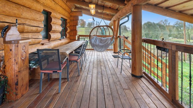 Een houten chalet met een veranda, een tafel, stoelen, een hangstoel en uitzicht op de omgeving.