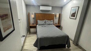 A hotel room with a bed, nightstands, a wall-mounted air conditioner, and a framed picture on the wall. - Hotel Colonial Inn  (Tijuana)