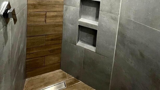 A modern bathroom with grey tiles, wooden wall paneling, and built-in shelves. - Hotel Colonial Inn  (Tijuana)