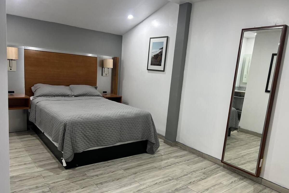 A bedroom with a bed, bedside tables, a mirror, and a picture on the wall.