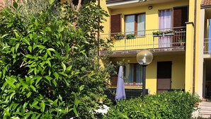 Un edificio giallo con un balcone, immerso nel verde.