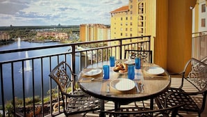 Un balcón con una mesa para dos, con vista a un cuerpo de agua y un paisaje urbano.