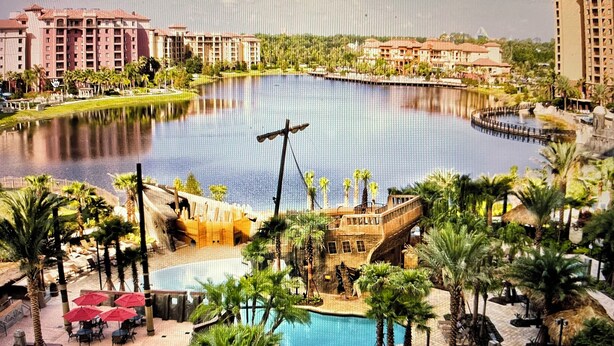 Un resort con una amplia piscina central, palmeras y un puente sobre el agua.