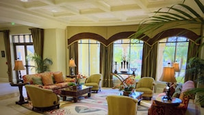 Un vestíbulo amplio con alfombra estampada, varias zonas de estar que incluyen sofás y sillones, una mesa de centro y una mesita de noche con lámpara.