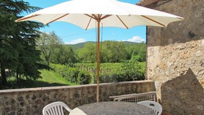 Une terrasse avec une table ronde et des chaises blanches, un parasol et une vue sur un vignoble.