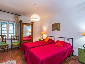 A room with two beds, a wooden wardrobe, a mirror, a lamp, and a window with curtains.