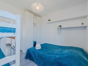 A bedroom with a bunk bed, a single bed with a teal bedspread, a hanging plant, and a ceiling light fixture. - Palmyra by Interhome (Le Barcarès)