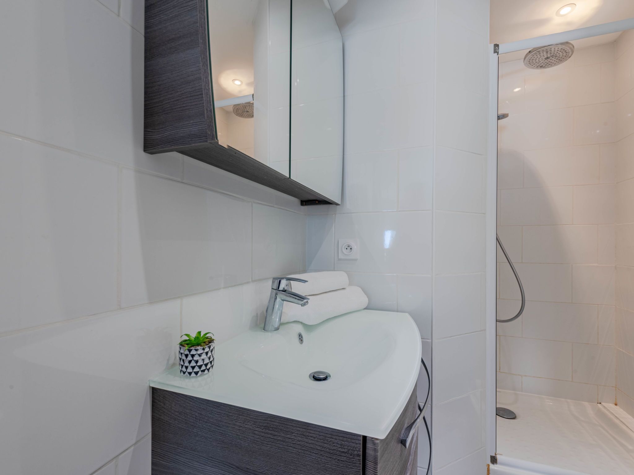 Casa de banho moderna com lavatório branco, espelho e chuveiro.
