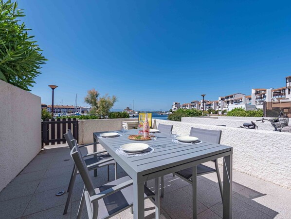An outdoor patio with a table set for dining, overlooking a marina and residential buildings. - Palmyra by Interhome (Le Barcarès)