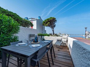 Un espace de restauration en plein air avec une table dressée pour quatre personnes, donnant sur une marina où sont amarrés des bateaux, et sous un ciel bleu dégagé.