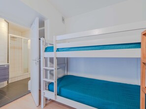 Une chambre avec des lits superposés, une zone douche et un petit placard.
