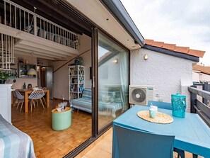 Amplia sala de estar con piso de madera, una mesa de comedor con sillas, un sofá y un amplio ventanal corredizo que da a un balcón exterior.