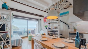 A modern kitchen with a wooden dining table set for four, white chairs, and a built-in bookshelf. - Antigua by Interhome (Le Barcarès)