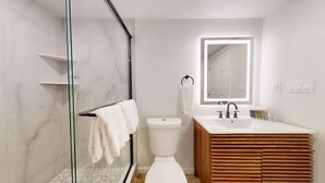 A modern bathroom with a glass shower enclosure, a white toilet, and a wooden vanity with a large mirror. - Comfortable Coastal Retreat with Two Queen Beds - Suite Room (Cape May)