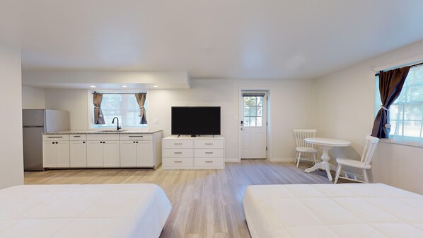 A hotel room with a kitchenette, a TV, a dining area, and two beds.