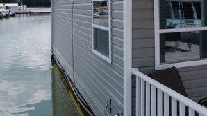 Una vivienda flotante con balcón, un muelle y un puerto deportivo al fondo.