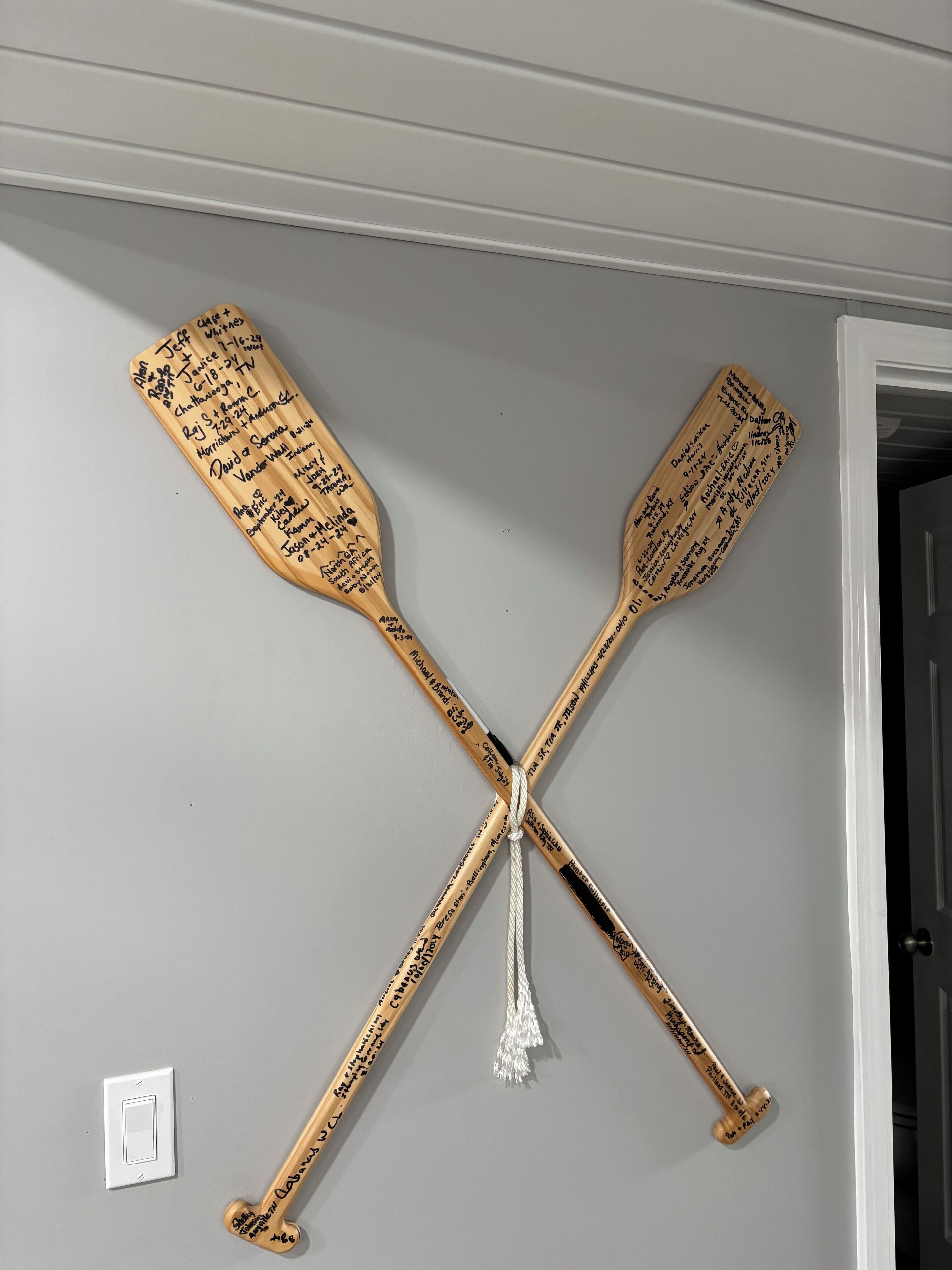 A wall-mounted wooden paddle with signatures, crossed over each other, and a tassel hanging from the center.