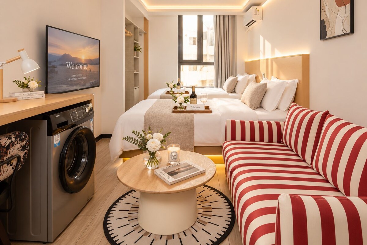 A hotel room with a bed, a sofa, a washing machine, a television, and a dining table.