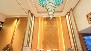 A reception desk with two laptops, a chandelier, and a large wall with intricate patterns. - Amanda Hotel (Phnom Penh)