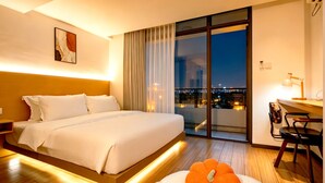 A hotel room with a large bed, a desk, a chair, a window with a city view, and a painting on the wall. - Amanda Hotel (Phnom Penh)
