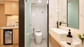 A modern bathroom with a glass shower enclosure, a white toilet, a sink with a large mirror, and a bottle of Aesop body wash.