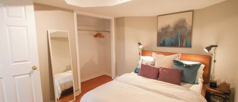A bedroom with a large bed, a wardrobe, a mirror, a nightstand, and a painting on the wall.