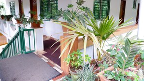 A staircase with a green railing leading to a landing area with potted plants and a red lantern. - WIND VALLEY FARMSTAY (Ramakkalmedu)