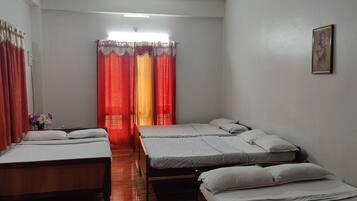 A hotel room with three single beds, a ceiling fan, and a window with red curtains.