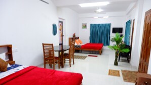A hotel room with a bed, a desk, and a chair. There is a television on the wall and a plant in the corner. - WIND VALLEY FARMSTAY (Ramakkalmedu)