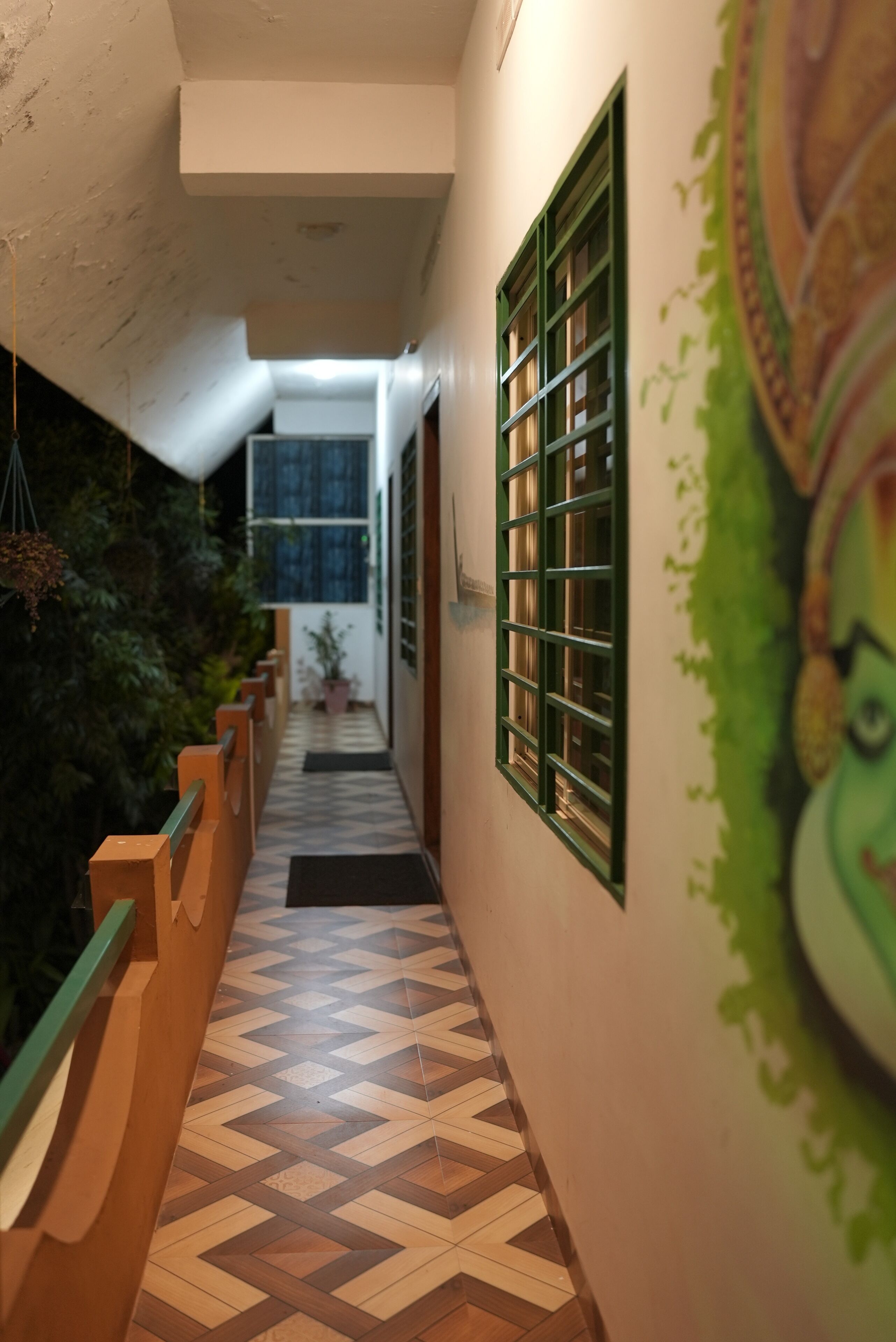 A corridor with patterned flooring, a green railing, and a wall with a decorative mural.