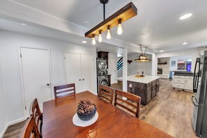 Een moderne keuken met witte kastjes, een centraal eiland en een eetgedeelte met een houten tafel en stoelen.