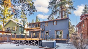 Une maison à deux étages avec une terrasse et un jacuzzi, située dans une cour enneigée.