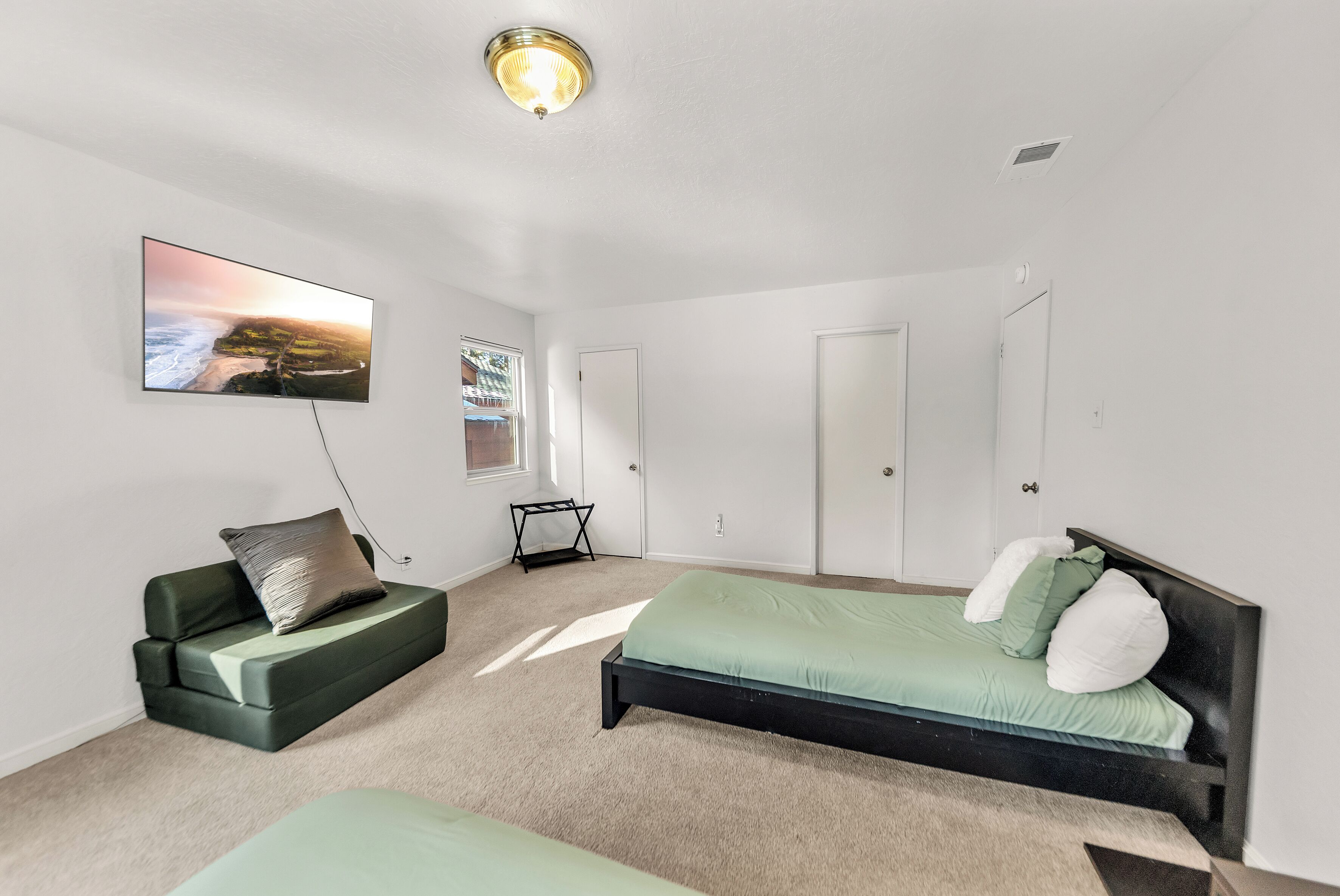 A bedroom with a bed, a sofa, a TV, and a window.