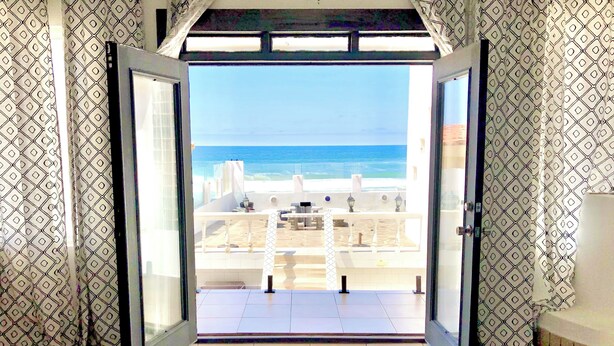 Habitació amb una gran porta corredissa de vidre que dona a un balcó amb vista a la platja i a l'oceà.