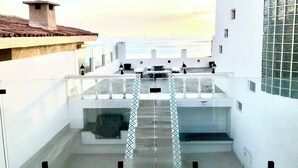 Terrassa al terrat amb vista al mar, amb barana blanca, taula petita i algunes cadires.