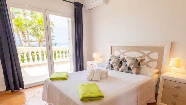 Ein Hotelzimmer mit Bett, zwei Nachttischen, einem Balkon und Blick auf Palmen.