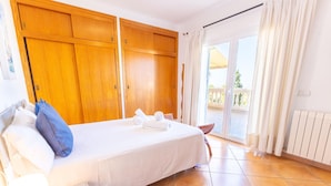 Ein Hotelzimmer mit Bett, Nachttisch, Stuhl, einer Schiebetür zu einem Außenbereich und einem Holzschrank.