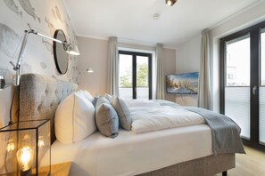 A modern bedroom with a large bed, a wall-mounted TV, and a balcony with curtains. - Sylt Marie - "Dreamlike vacation apartment Sylt Marie - relaxation and recreation (Wenningstedt-Braderup (Sylt))