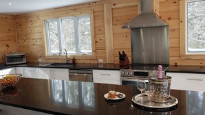 Eine moderne Küche mit Holzwänden, einer Edelstahl-Dunstabzugshaube und einer großen Kochinsel mit einer Glas-Schüssel und einer Champagnerflasche.
