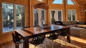 Eine geräumige Holzhütte mit großem Esstisch, schwarzen Stühlen und einer gemütlichen Sitzecke.