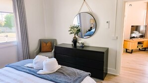 A bedroom with a bed, a dresser, a mirror, a chair, and a desk.