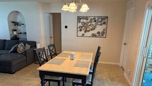 Un coin repas avec une table en bois, des chaises noires et un élément décoratif en métal fixé au mur.