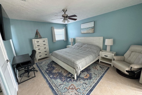 King-size bed with sheets, blanket, and pillows. Comfortable sitting chair.