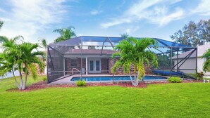 Une maison avec une piscine dans le jardin, un patio couvert et un espace clos agrémenté de palmiers.