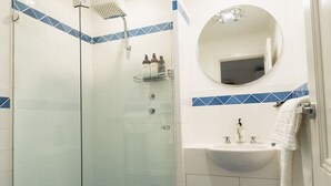 Un baño moderno con ducha envuelta en vidrio, un espejo redondo y un lavamanos blanco con una toalla colgada en la pared.