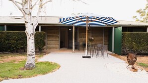 Una cabaña de troncos con un patio que cuenta con una sombrilla a rayas, mobiliario exterior y un árbol.
