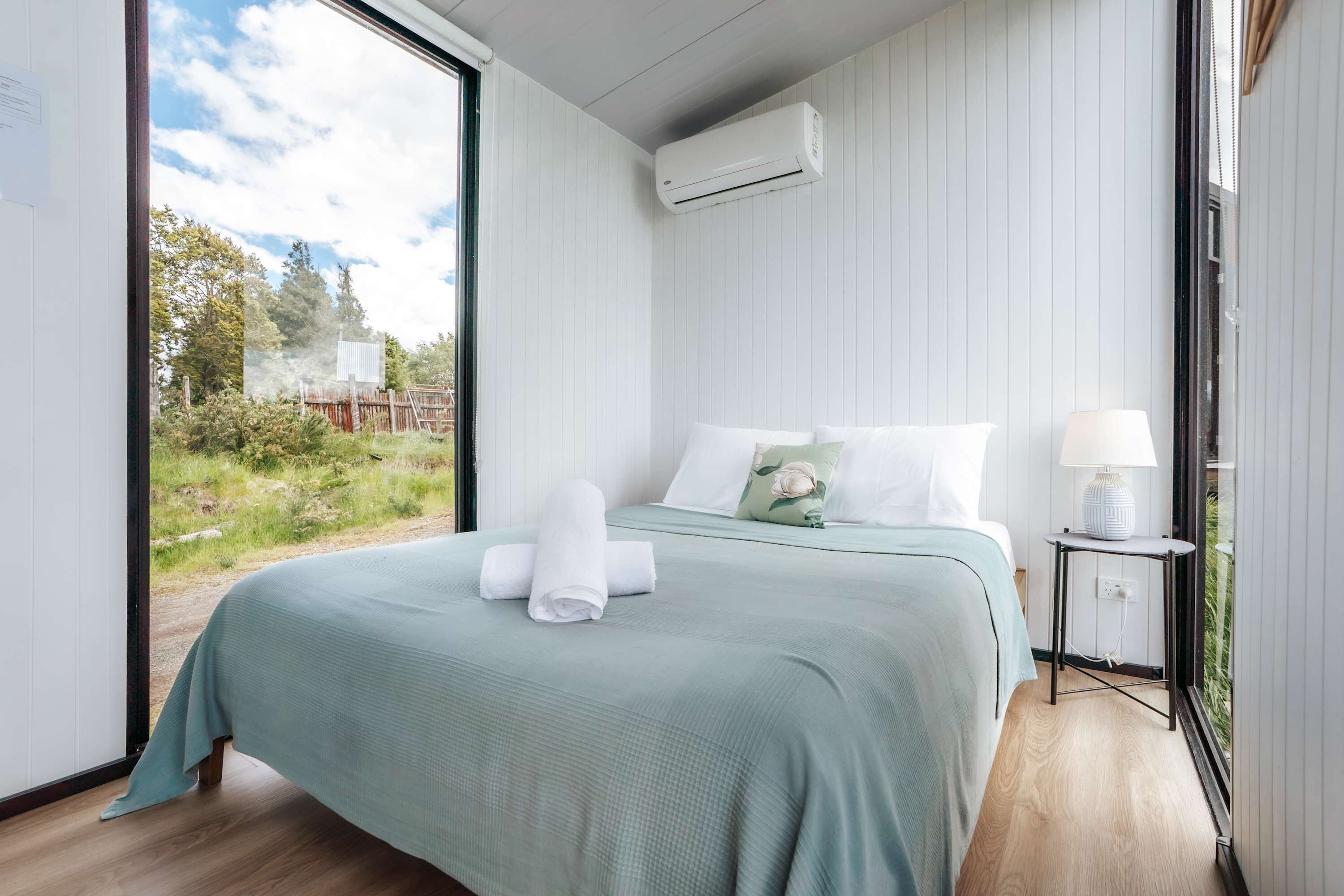 Une chambre à coucher avec un lit, une table de chevet avec une lampe, et une vue sur la verdure à l’extérieur.