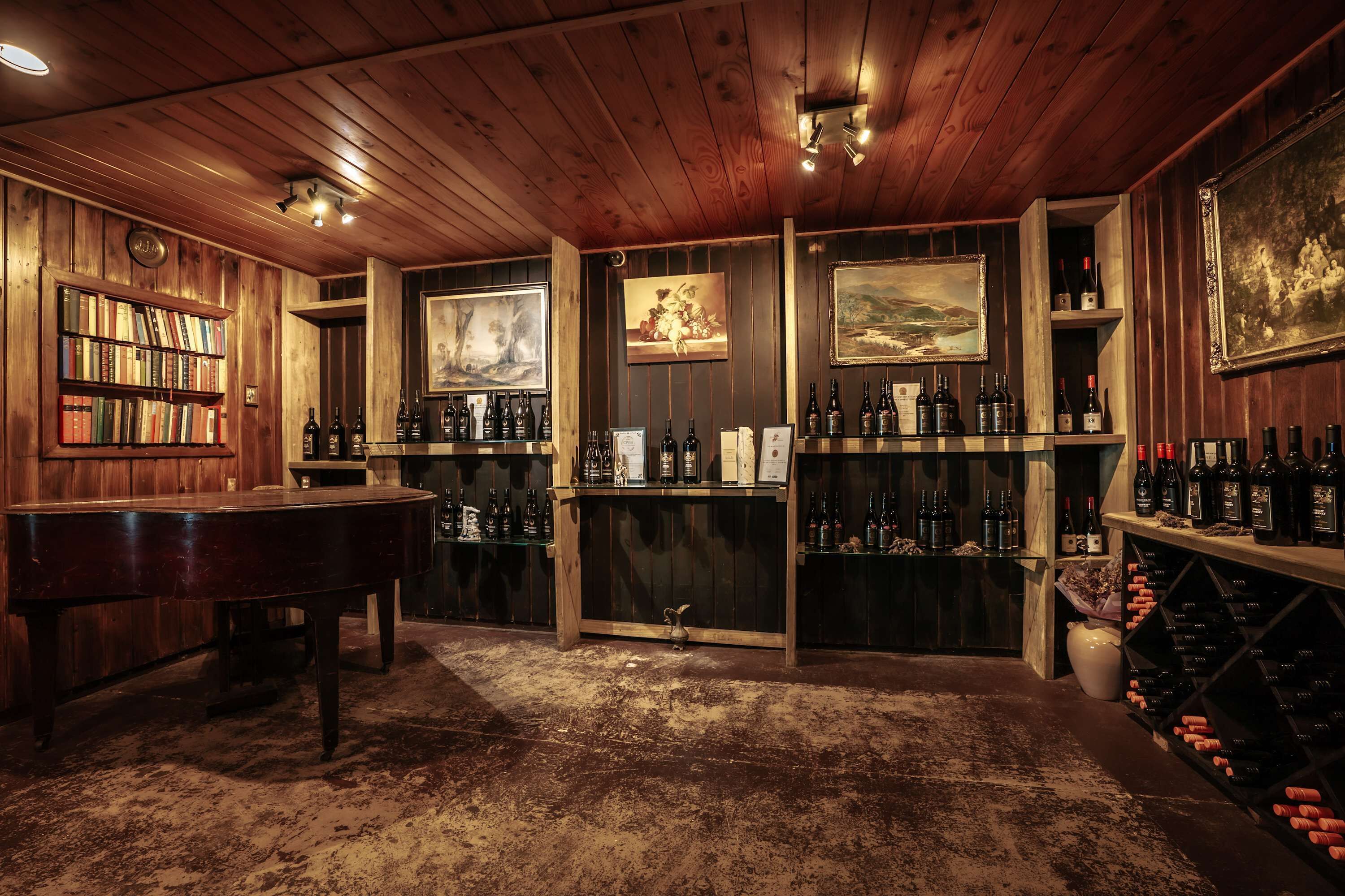 A wooden-paneled room with a piano, bookshelves, wine racks, and framed artwork.