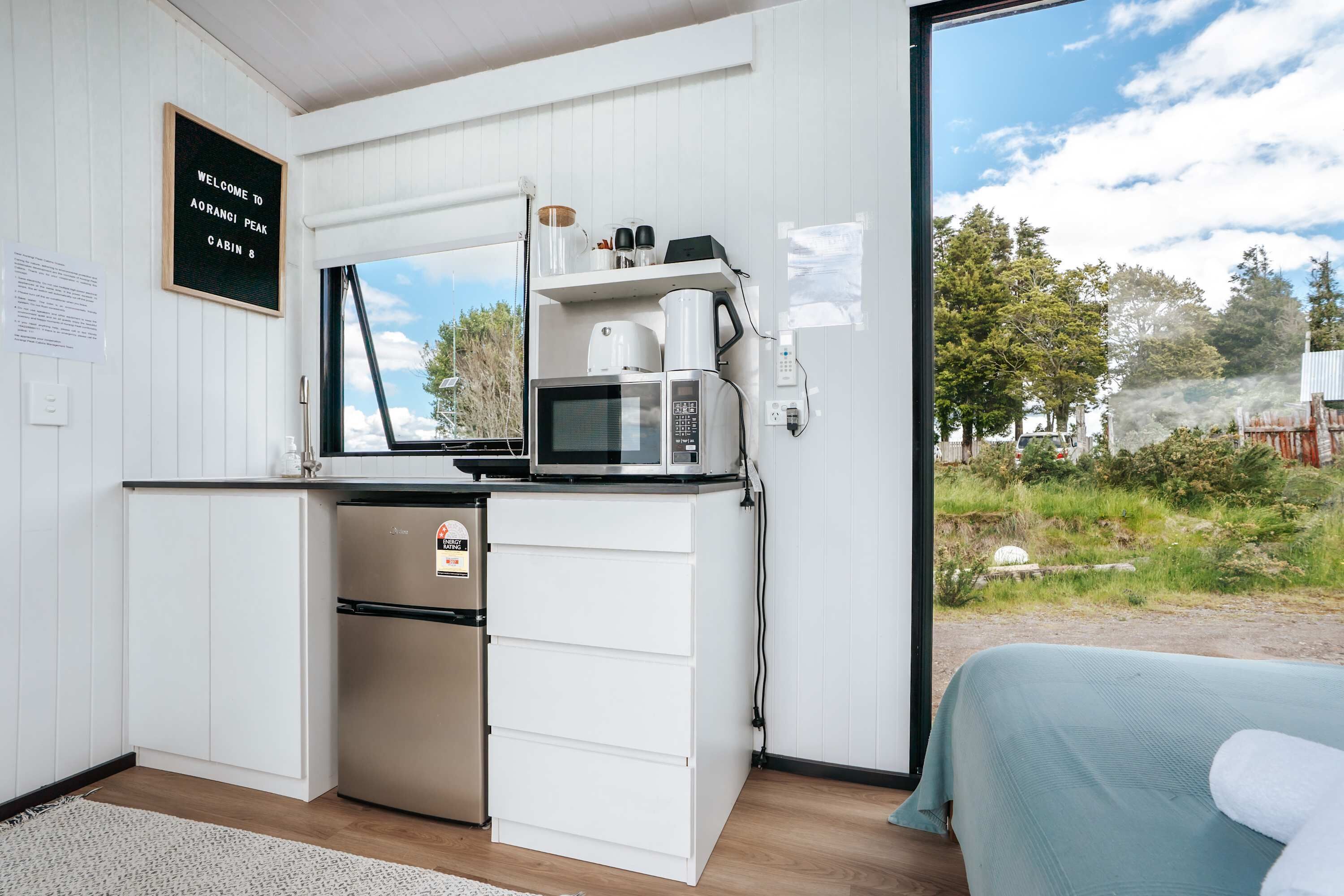Eine Hütte mit einer Küchenzeile, einem Bett und Blick ins Freie.