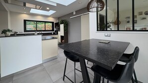 A modern kitchen with a central island, a dining area with a dark table, and a skylight above.